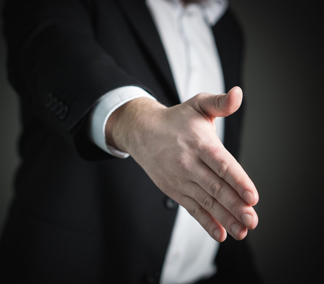 A businessman in a dark suit extends his hand to shake on a partnership